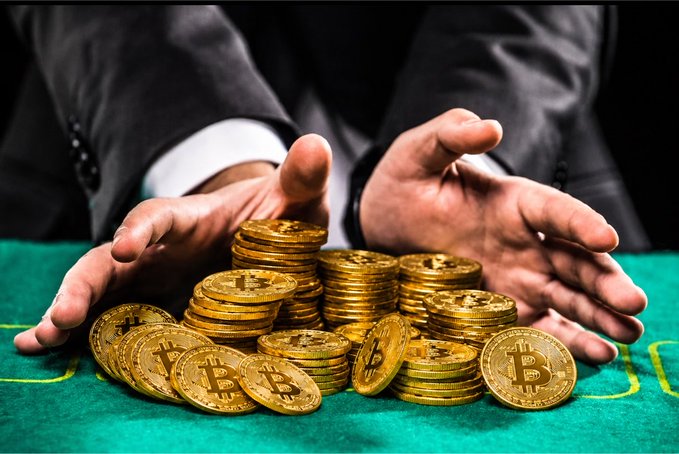 A person in a suit gestures over a pile of gold Bitcoin tokens on a green felt surface, visually reinforcing their bold wager on Bitcoin reaching $500K. The image's focus on a fortune in Bitcoin coins underscores the high-stakes confidence of the claim.