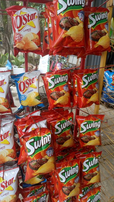 A retail display rack filled with hanging bags of 'O'Star' and 'Swing' brand potato chips in red, white, and blue packaging.