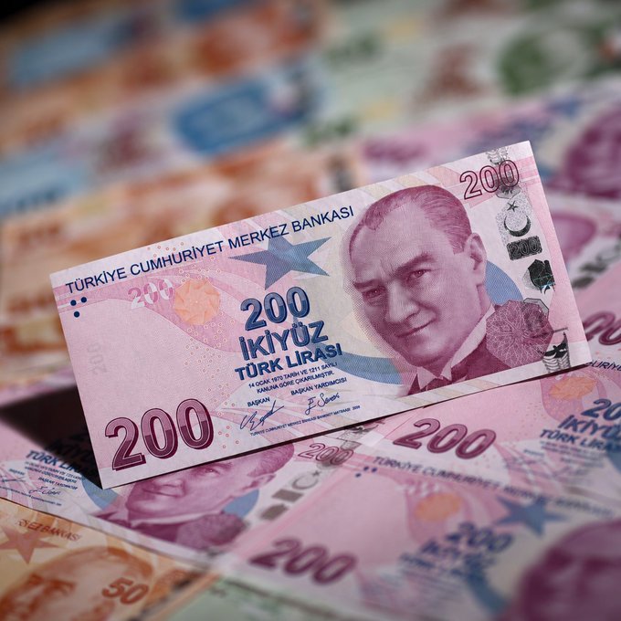 A 200 Turkish lira banknote from the "TÜRKİYE CUMHURİYET MERKEZ BANKASI" featuring Mustafa Kemal Atatürk rests atop scattered lira bills, visually representing the currency's dramatic depreciation against Bitcoin as highlighted in the post.