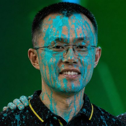 The image features a man with blue paint splattered all over his face, including his glasses. The man appears to be smiling for the camera while wearing the blue paint splatters. The caption of the image reads "@BINANCE TO BE BANNED FROM EUROPE THATS NOT EGG ON HIS FACE #CROFAM @cryptocom @kris @fwiz @cronosapp @aidotcom $BTC $ETH $MCGA $CRO #crofam #crypto". The man's face is the main focus of the image, with the blue paint splatters adding a unique and artistic touch to his appearance.