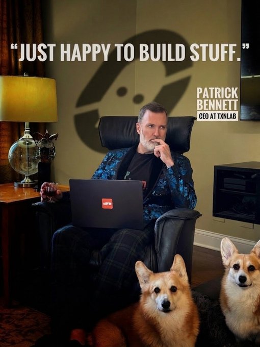 Promotional photo of Patrick Bennett, CEO at TXNLab, sitting with a laptop and two corgis, with quote 'JUST HAPPY TO BUILD STUFF.' and a TXNLab logo in the background.