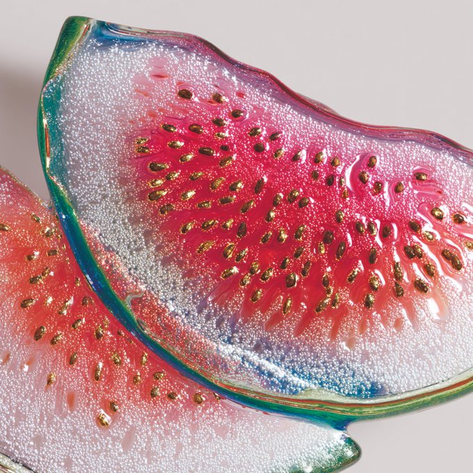 Close-up of a decorative glass watermelon slice ornament with pink/red flesh, gold seeds, white rind with bubbles, and a colorful green-blue-green edge, designed as a ring dish.
