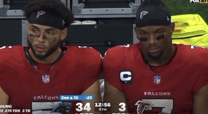 Two Atlanta Falcons players, identified by the on-screen graphic as "YOUNG" with "275 YDS 3 TD", sit on the bench looking disappointed during a game where they are losing 34 to 3.