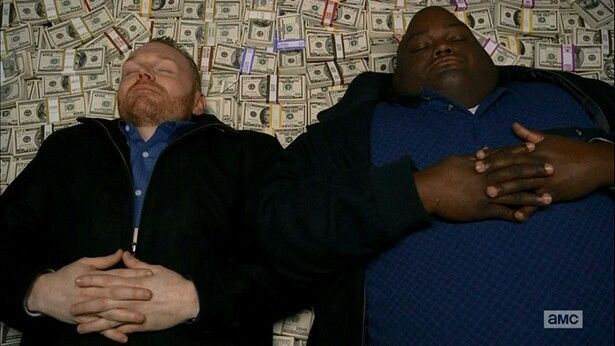 A promotional still from AMC showing two men lying on a pile of money with their hands folded over their chests, with the AMC logo in the bottom right corner.
