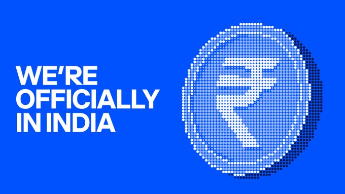The image features a blue background with a white circle containing a coin icon, which has the text "We're officially in India" written above it. The text is in all capital letters, making it stand out against the blue background. Below this, there's an inline advertisement for Coinbase, encouraging users to use their INR rails to access the cryptocurrency exchange platform.