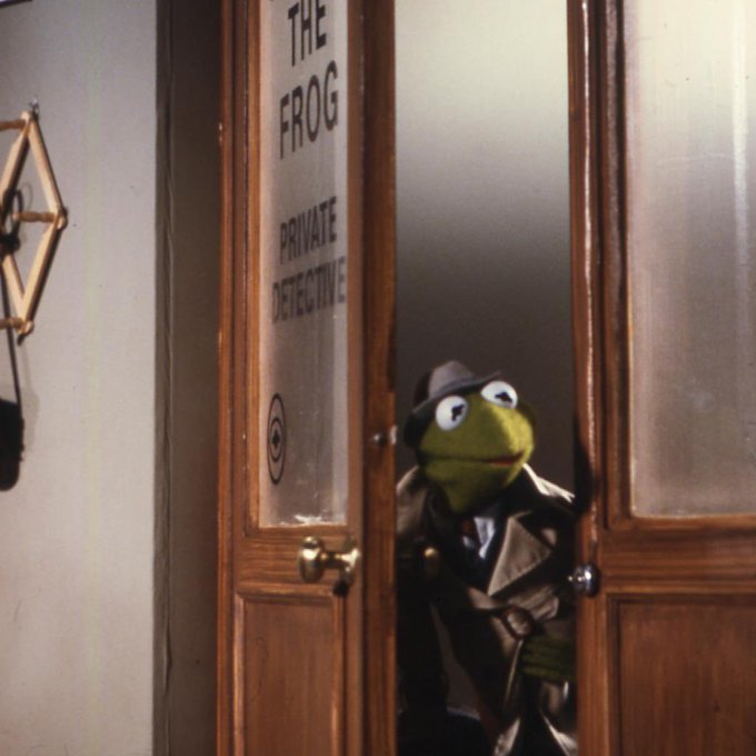 Kermit the Frog, dressed as a detective in a trench coat and fedora, peeks through a wooden door marked 'THE FROG PRIVATE DETECTIVE'.