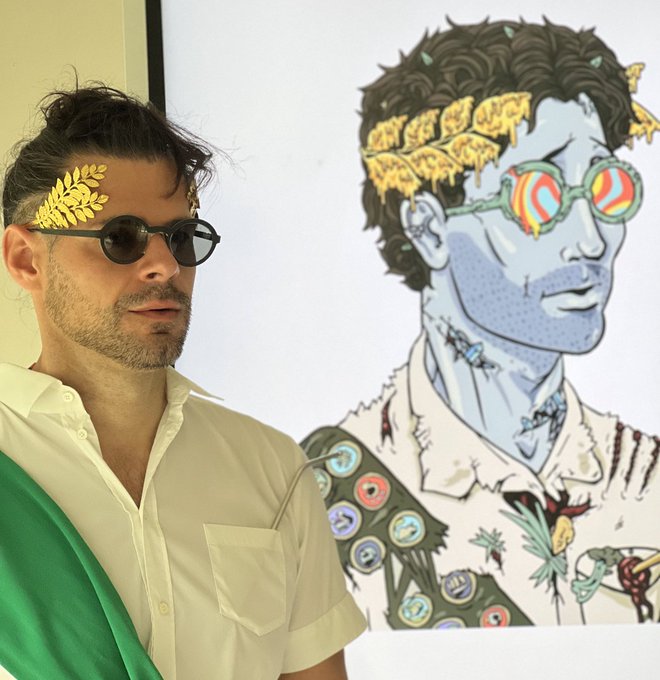 A man with sunglasses and a gold laurel leaf headpiece stands next to a stylized illustrated portrait featuring similar sunglasses and colorful text on the forehead.