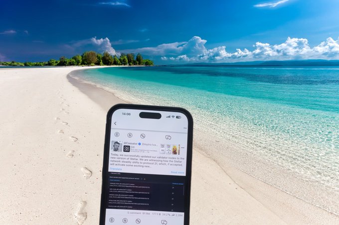 A smartphone displaying a social media feed rests on white sand along a turquoise beach with footprints leading toward the water.
