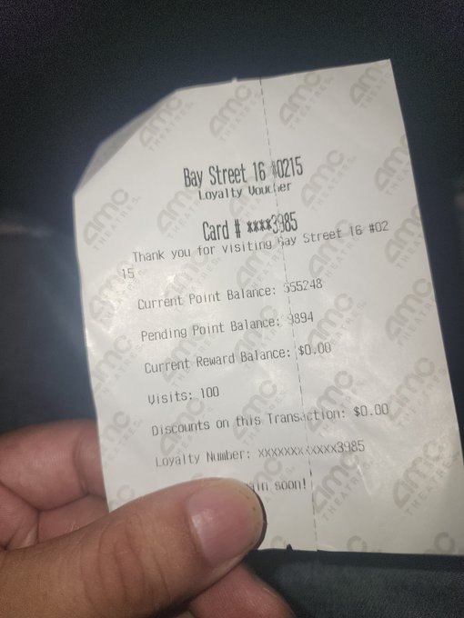 A hand holding an AMC Theatres loyalty voucher receipt from Bay Street 16 #0215, showing a card number ending in 3985 and over 35,000 loyalty points.