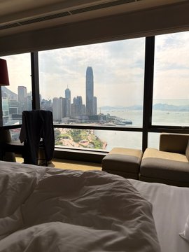 A hotel room view overlooking a waterfront cityscape with a prominent skyscraper, paired with the caption "Crypto made this happen," suggesting the travel was funded by cryptocurrency gains.