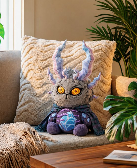 The image features a stuffed animal, possibly a teddy bear or a plush toy, sitting on top of a couch cushion. The stuffed animal has large horns and a blue scarf wrapped around its neck. In front of the stuffed animal, there is a book placed on the couch. The background includes a window with blinds that allow natural light to enter the room, as well as a potted plant located next to the window. The image also contains text that reads "Loading ApeCoin..." and "Focus on what is in the image and how it relates to the post."