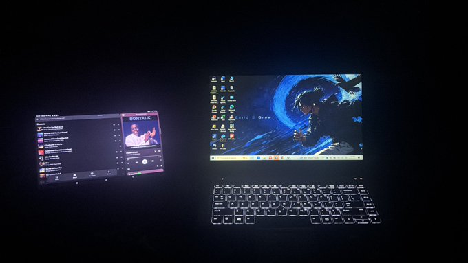 Two virtual screens float above an illuminated keyboard in a dark room, with the left display showing a music playlist and the right desktop displaying a blue dragon wallpaper labeled "David" and "Grey" alongside a Windows taskbar. This futuristic tech setup ties into the celebratory post marking a contest victory ("Took first out of 99 entries") thanking @claimrushdev, suggesting the dual-monitor workstation represents the productivity tools that helped secure the win.