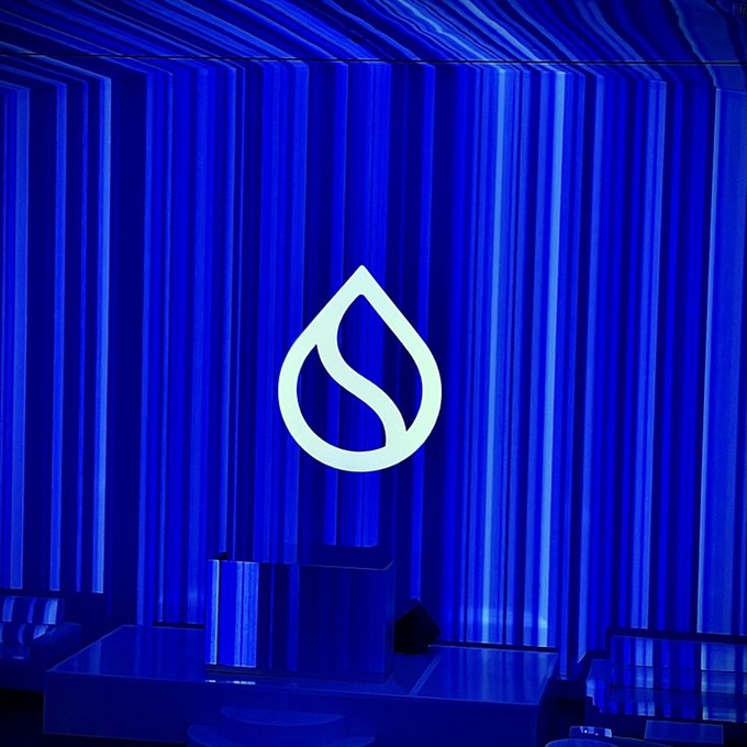 A large, illuminated Sui logo glows against a backdrop of vertical blue light strips on a stage.