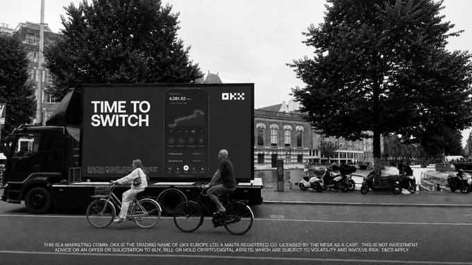 A mobile digital billboard truck displays an OKX advertisement reading "TIME TO SWITCH" with the headline "4,381.62..." alongside an OKX-branded app interface, parked on a city street as cyclists ride past. The image visualizes OKX's promotional campaign highlighting their trading platform, X-Perps, and the benefits of becoming a VIP for lower fees on both perpetual and spot trading.