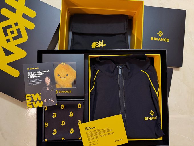 A Binance SVB Global Swag Ambassador Campaign merchandise box containing a black hoodie with Binance branding, a yellow plush toy, and promotional materials.