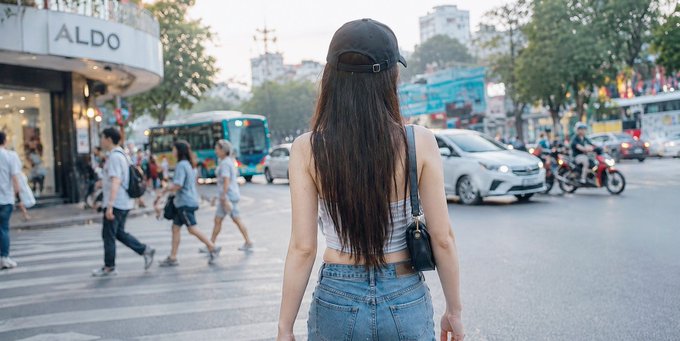 The image shows a woman walking down a street with her back turned towards the camera. She has long hair, blue jeans, and a black hat on her head. The background of the photo features several people walking around, as well as cars and buses in the distance. There is also a bus stop visible near the center of the image.

The post includes text that reads "Mình đây hệ sinh thích @base thời gian gần đây. Hệ sinh thái phát triển mạnh, trải nghiệm mượt mà. Nghe tin team đây có token riêng rìng hình vẫn build đân lý nè. Base đã đây". The woman in the image is walking away from the camera, and there are several other people visible in the background as well.
