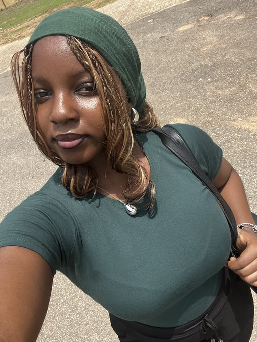 A selfie of a woman wearing a green headband and matching green top, with long braids and a black shoulder bag.