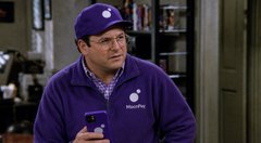 A man wearing glasses, a purple beanie, and a purple 'Insightful' branded zip-up jacket, holding a purple mug in what appears to be a retail store setting.