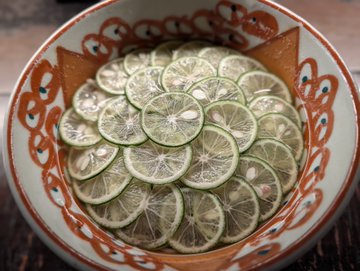 A decorative ceramic bowl filled with sliced green citrus fruit (likely sudachi or kabosu) is shown from above.