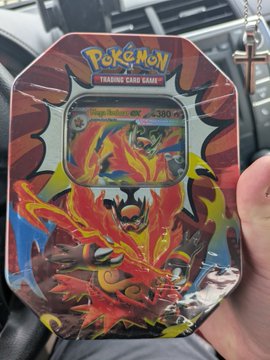 A Pokémon Trading Card Game blister pack featuring Magikarp & Wailord-GX, held in a hand inside a car with a cross charm hanging.