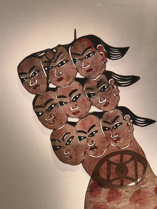 An artistic illustration featuring multiple overlapping faces with stylized features and dark hair, arranged in a clustered composition on a beige background.