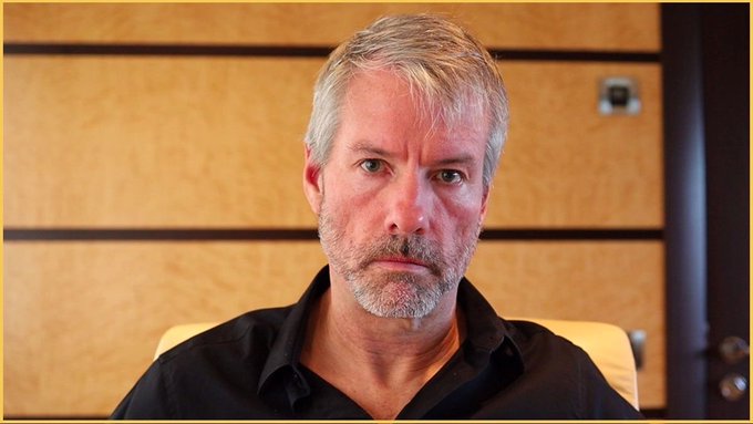 In the image, there's a man sitting down with his arms crossed over his chest. He has a beard and appears to be focused or serious about something. The photo was taken at a time when the Bitcoin market experienced a significant decline, as indicated by a caption that reads "STRATEGY IS DOWN OVER 10% SINCE SELLING BITCOINYESTERDAY". The man's demeanor and body language could suggest that he is contemplating his investments or reacting to the current situation in the cryptocurrency world.