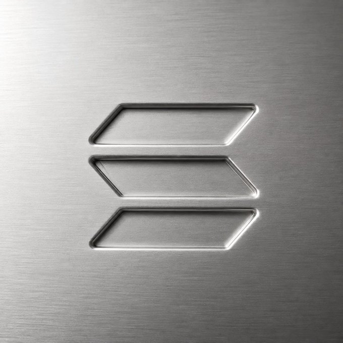 A close-up of a brushed metal surface featuring three stacked hexagonal/chevron-shaped engraved outlines, resembling a stylized logo.