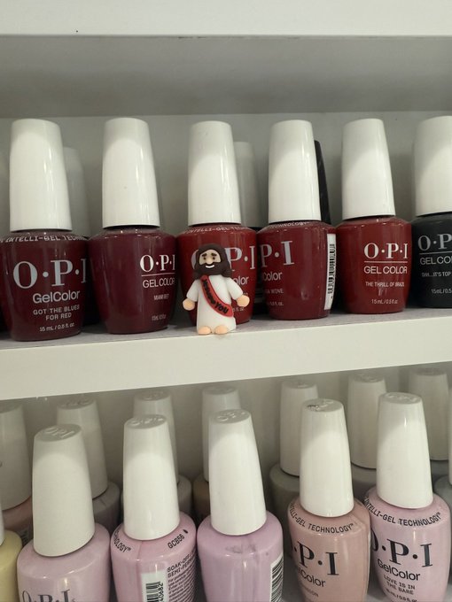 A small "I Voted" figurine stands on a store shelf among rows of OPI GelColor nail polish bottles in shades of red and light purple.