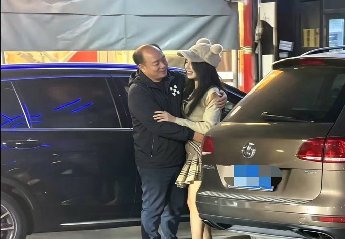 An older man in a black jacket warmly embraces a young woman wearing a beige cap and plaid skirt between two SUVs in what appears to be a parking garage, with the post humorously questioning the scene as someone's lavish "OKX VIP" lifestyle moment.