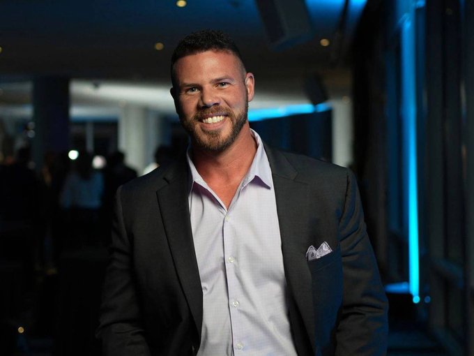 A bearded man in a dark blazer and light purple dress shirt smiles confidently at what appears to be a formal event with blue-lit décor. The "$XRP" post likely connects the image to a public figure associated with the Ripple cryptocurrency ecosystem.