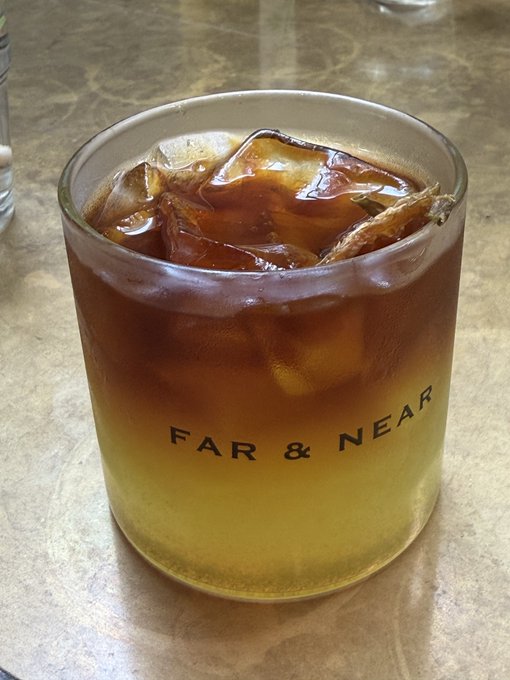 A glass containing a layered iced coffee or tea drink sits on a marble surface, with the text 'FAR & NEAR' printed on the glass.