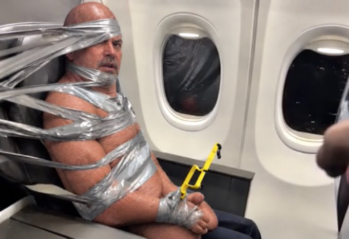 A humorous meme-style image showing a bald, muscular man sitting in an airplane seat wrapped extensively in silver duct tape while holding a yellow plastic object, appearing bewildered.