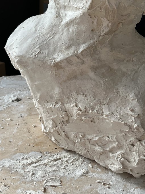 A rough, textured mass of light gray clay or plaster sitting on a wooden surface with loose debris around it.