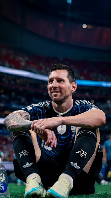 Lionel Messi in Argentina's blue and black World Cup kit sitting on the field after a match.