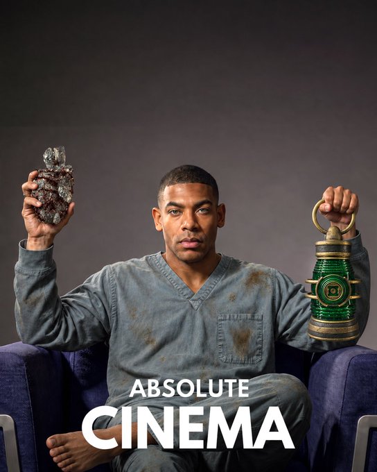A man with a dirt-smudged scrubs sits cross-legged on a blue couch, holding up a green Lantern power battery in one hand and a dark rock in the other, with the text "ABSOLUTE CINEMA" overlaid at the bottom.

The image humorously ties into the post's reference to "Lanterns" by depicting the man holding a Green Lantern power battery like a trophy, jokingly treating a domestic victory over an ex-husband as an epic, cinematic hero moment worthy of a superhero's prized possession.