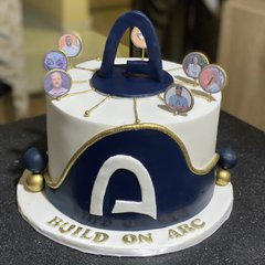 A custom white and navy blue cake decorated with gold accents and small character photos, featuring the letters 'A' and the text 'BUILD ON ABC' on the base.