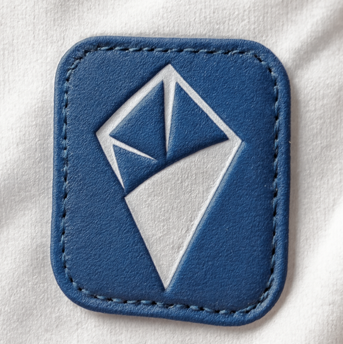 A blue leather patch with stitched edges featuring an embroidered white diamond or crystal logo sewn onto white fabric.