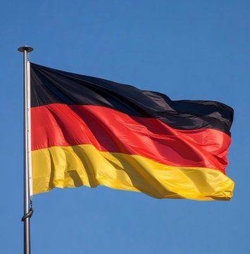 The German national flag (black, red, and gold horizontal stripes) waving on a flagpole against a clear blue sky.