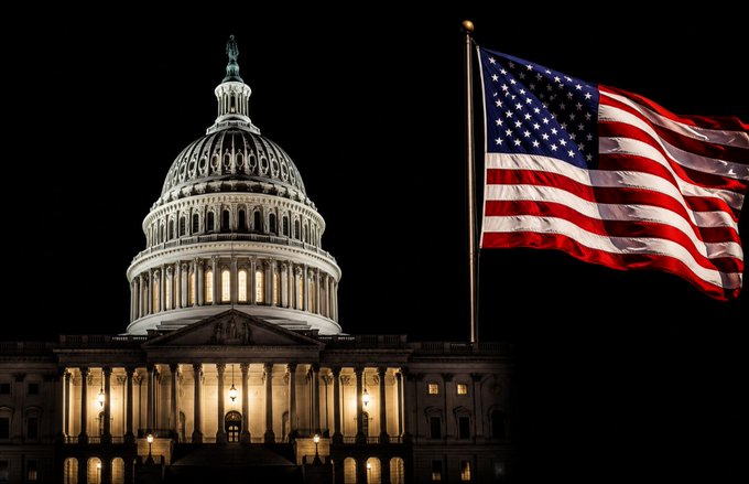 The U.S. Capitol building stands illuminated at night, with an American flag waving prominently in the foreground, symbolizing the legislative action taking place on the CLARITY Act as the Senate faces a critical deadline before the August recess.