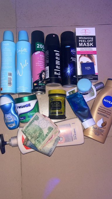 An assortment of personal care products, toiletries, cosmetics, and currency is scattered on a tiled floor.