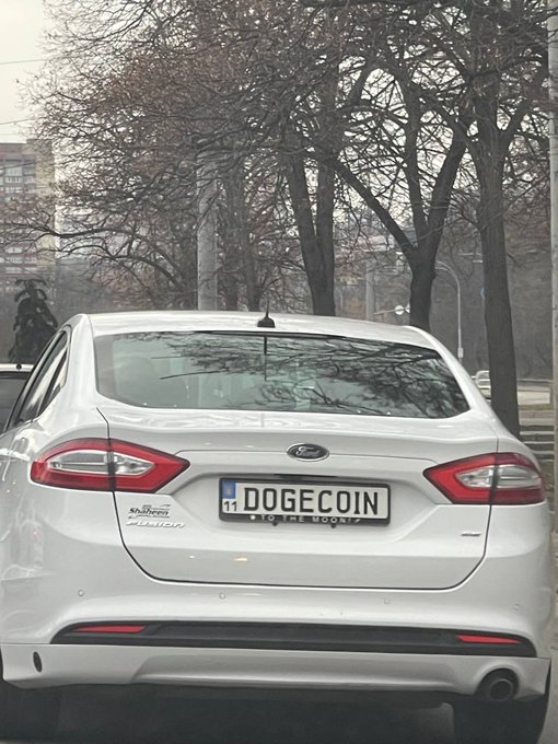 The rear view of a white Ford Mondeo car parked on a street, featuring a custom license plate that reads 'DOGECOIN.'