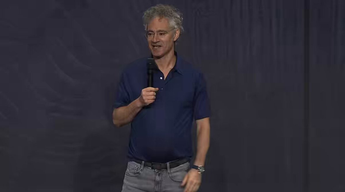 The image features a man standing in front of a black background with his hands up. He appears to be speaking into a microphone or giving a presentation, as he holds a microphone close to his mouth. The caption above him reads "Without pltr ontology, businesses find themselves burning one years of token in months and get some AI slop." This suggests that the man might be discussing the importance of maintaining a strong online presence for businesses, particularly in terms of social media management and content creation.