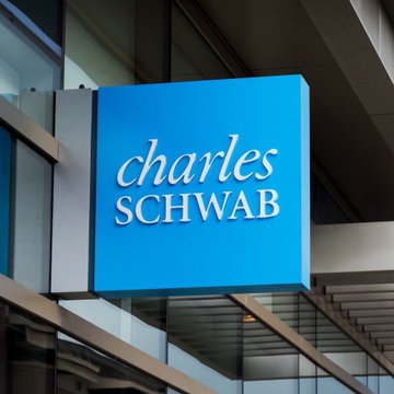 A Charles Schwab corporate sign is displayed outside an office building, with the company name "charles SCHWAB" written in white text on a bright blue square sign. The image directly relates to the news, as the sign represents the firm that has disclosed $4.8M in XRP ETF shares as collateral across multiple ETF issuers.