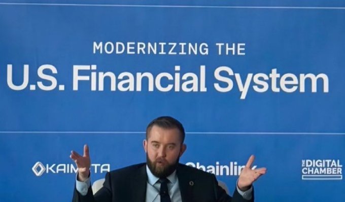 A bearded man in a suit gestures with both hands while speaking at a 'Modernizing the U.S. Financial System' event with Kaimeta, Chainlink, and The Digital Chamber logos visible.