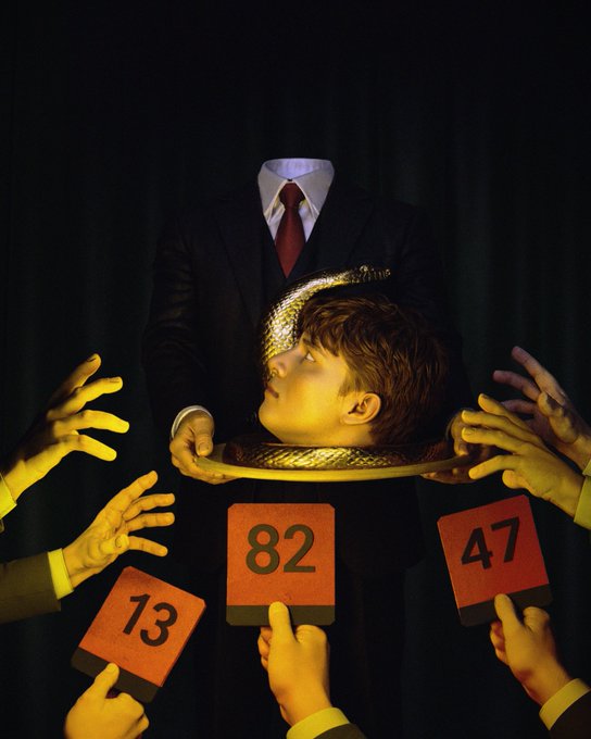 A surreal photograph of a child's head on a silver platter held by a headless figure in a suit, surrounded by multiple hands holding up scorecards reading '13', '82', and '47'.