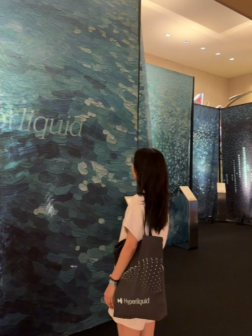 A young woman with long dark hair stands viewing large blue, textured art panels labeled 'Liquid' and 'Hyperliquid' in a gallery setting.