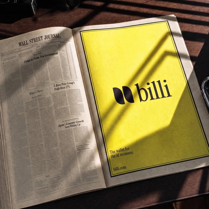 A newspaper opened to a full-page yellow advertisement for 'billi', described as 'The wallet for the AI economy' with the website billi.com, sitting next to standard Wall Street Journal articles.