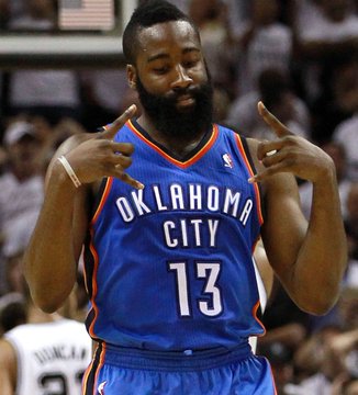 Basketball player James Harden, wearing an Oklahoma City jersey with the number 13, makes a gesture with both hands during a game.