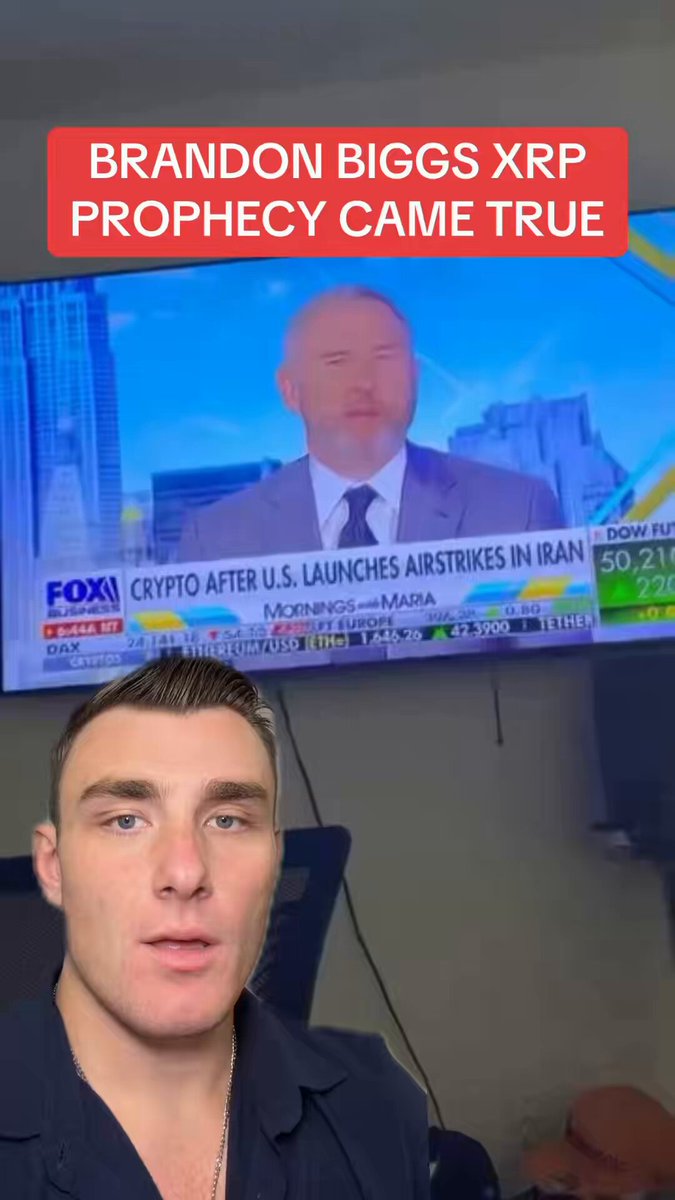 The image features a man sitting at his desk with a TV screen behind him displaying an advertisement for Bitcoin. The text on the screen reads " Brandon Biggs XP PROPHETIC WORDS ARE COMING TO PASS RIGHT INFRONT OF OUR EYES AS WE SPEAK... @BrandonBiggs247 was right!!!". This suggests that the man is discussing or promoting Bitcoin, and he might be sharing his thoughts about the cryptocurrency with others.