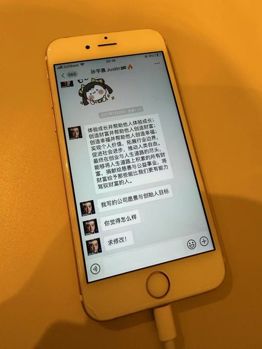 A gold iPhone rests on a wooden desk, displaying a WeChat conversation with "Sun Yuchen Justin" (孙宇晨) where he discusses an entrepreneurship project about body elongation and wealth redistribution. The image relates to the post by showing Justin Sun's flamboyant messaging style, fitting his reputation for self-promotion and grandiose projects.